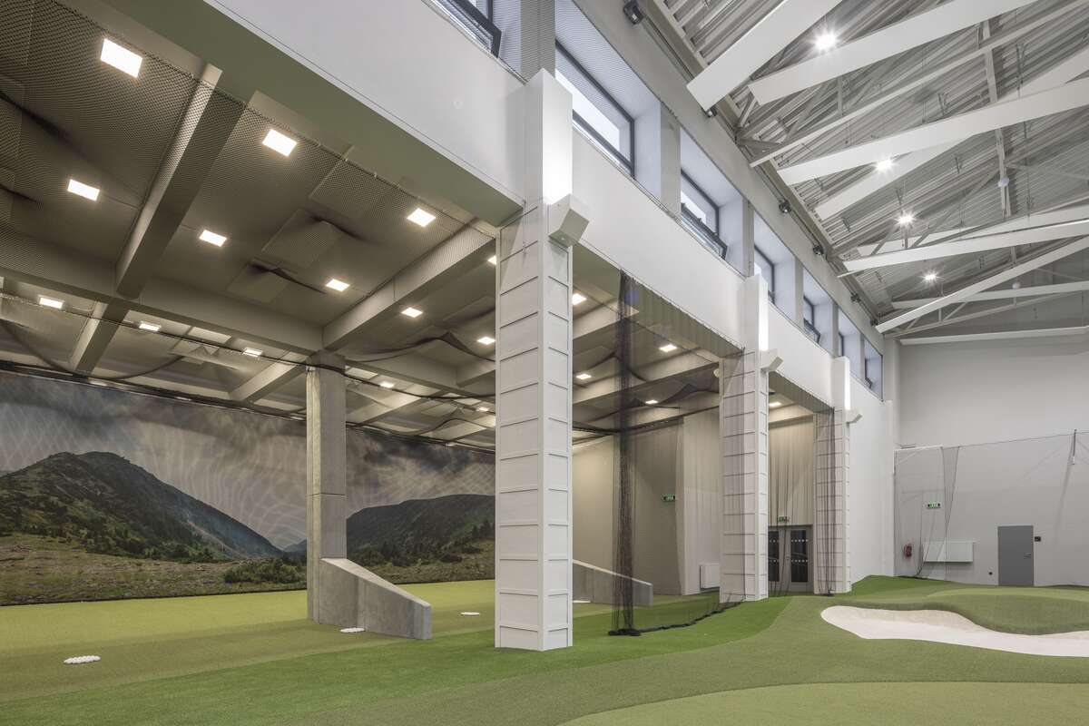 Tréninková plocha Golf Areny s bunkerem, ochrannými sítěmi a odpalovacími boxy pod původním betonovým skeletem